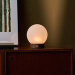 Oplaadbare tafellamp Flore in donkerbruin hout met bolvormige glazen kap op houten dressoir