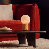 Flore oplaadbare tafellamp met lichtbruin houten voet en ronde glazen bol op een zwarte salontafel