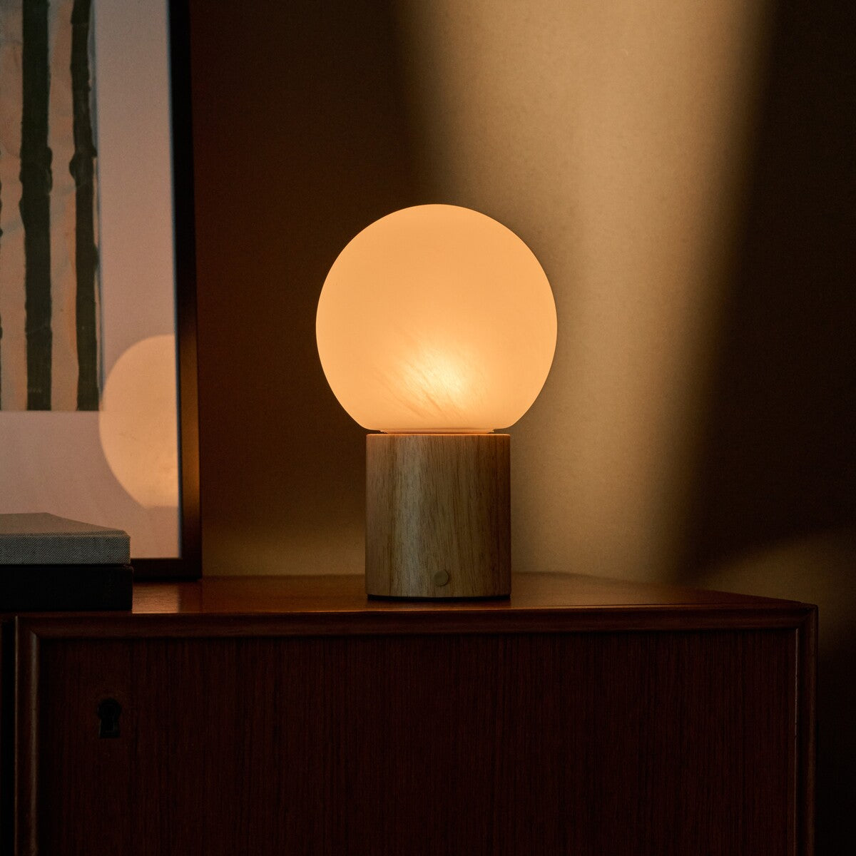 Flore oplaadbare tafellamp met lichtbruin houten voet en glazen bol op een houten dressoir