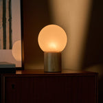 Flore oplaadbare tafellamp met lichtbruin houten voet en glazen bol op een houten dressoir
