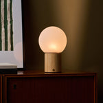 Flore oplaadbare tafellamp met lichtbruin houten voet gloeiend op een donker houten kastje