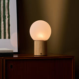 Flore oplaadbare tafellamp met lichtbruin houten voet gloeiend op een donker houten kastje