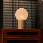 Oplaadbare tafellamp Flore Medium lichtbruin hout met glazen bolkap op een houten dressoir