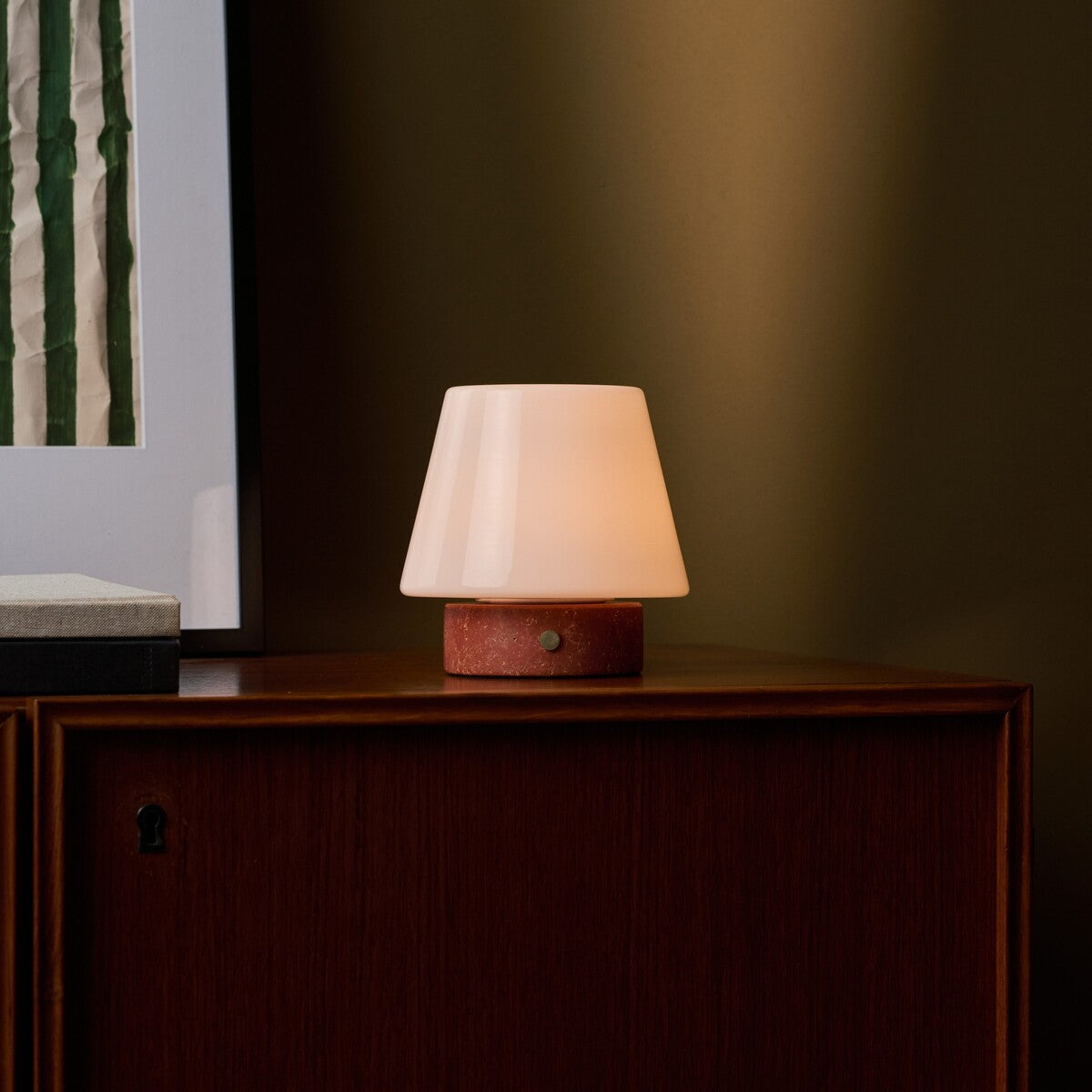 Oplaadbare tafellamp Hooch Small met rode Travertine marmeren voet tegen olijfgroene muur