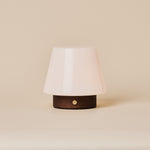 Tafellamp oplaadbaar Jadey donkerbruin hout gloeiend naast een rode gebloemde fauteuil