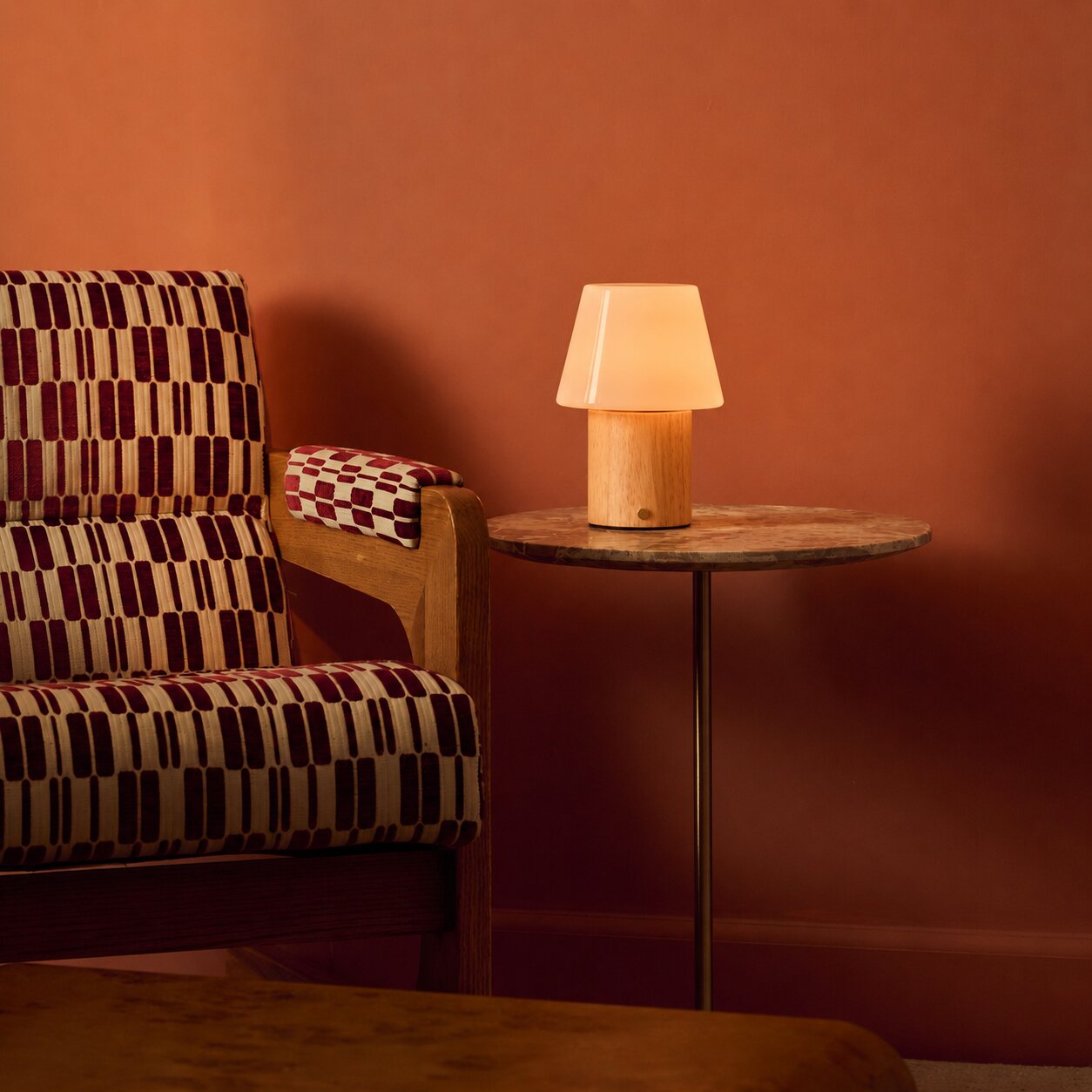 Cordless table lamp Jadey Medium in light wood with opal glass shade beside checkered armchair