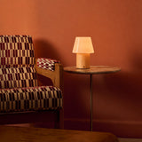 Cordless table lamp Jadey Medium in light wood with opal glass shade beside checkered armchair