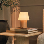 Rechargeable table lamp Jadey Medium, wood base and glass shade on side table with books and plant