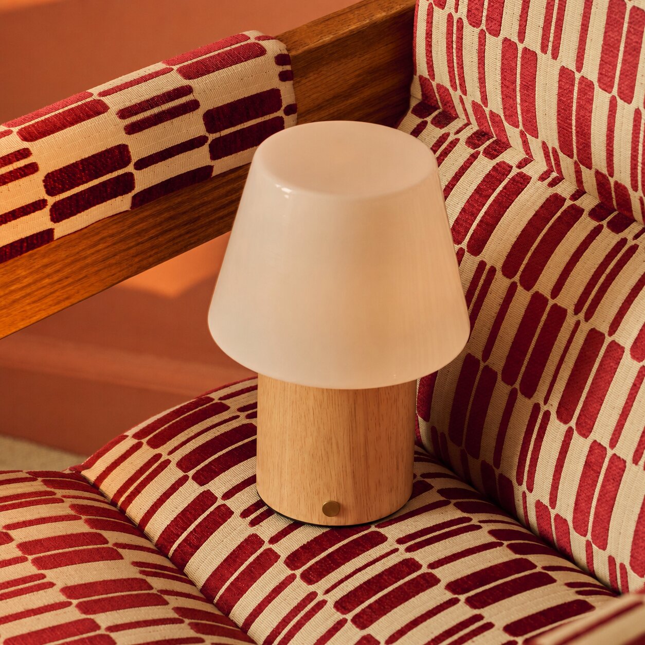 Cordless table lamp Jadey Medium, light wood base with opal glass shade on red patterned armchair