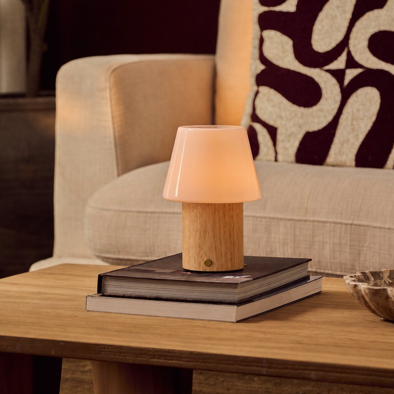 Rechargeable table lamp Jadey Medium, wood base with glass shade on coffee table beside beige armchair