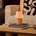Rechargeable table lamp Jadey Medium, wood base with glass shade on coffee table beside beige armchair
