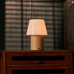 Cordless table lamp Jadey Medium in light wood and glass shade on bedroom nightstand near blinds