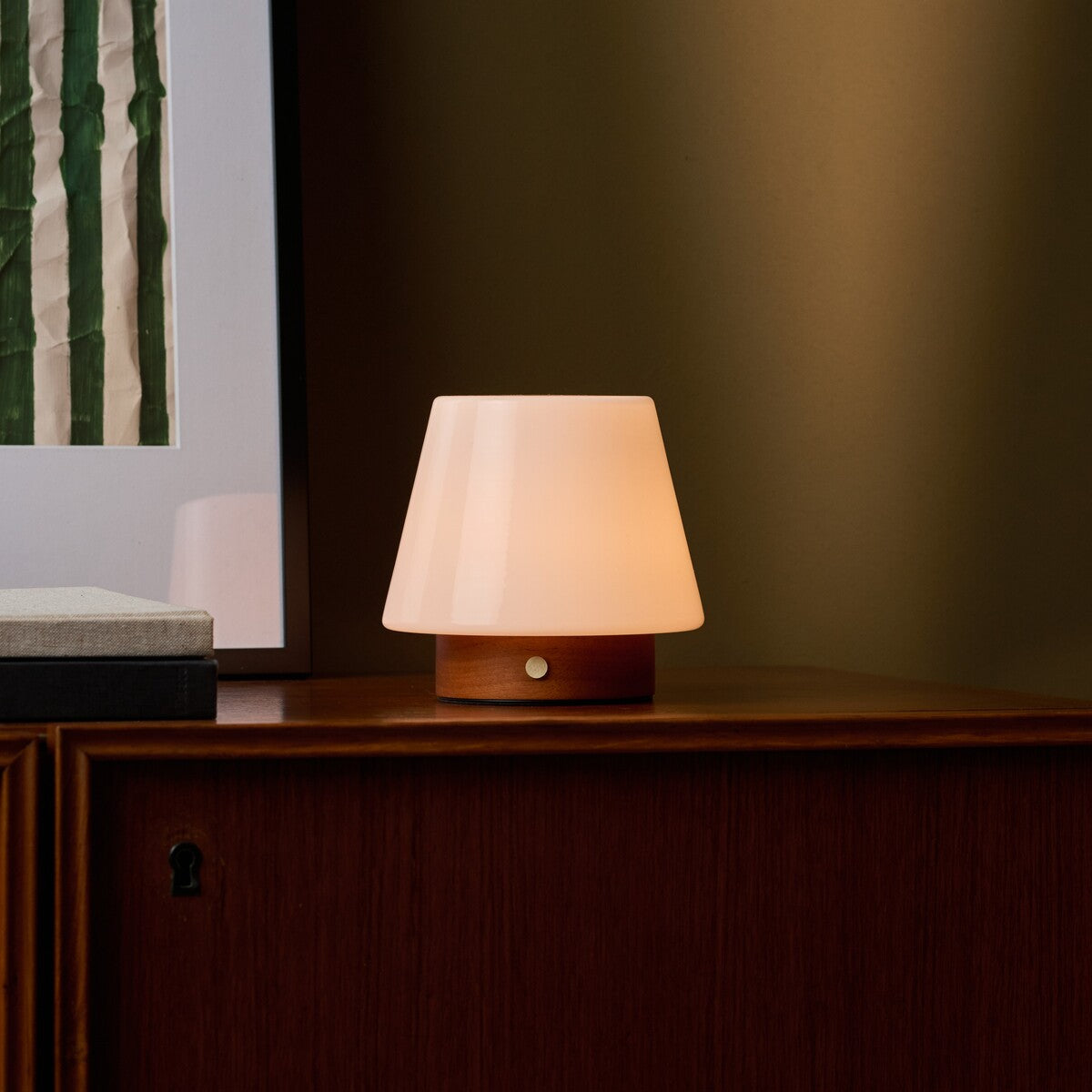Oplaadbare tafellamp Jadey Small kastanjebruin hout, brandend op houten dressoir naast kunstwerk