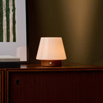 Oplaadbare tafellamp Jadey Small kastanjebruin hout, brandend op houten dressoir naast kunstwerk