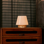 Oplaadbare tafellamp Jadey Small, hout met glazen kap brandend op donkere houten ladekast