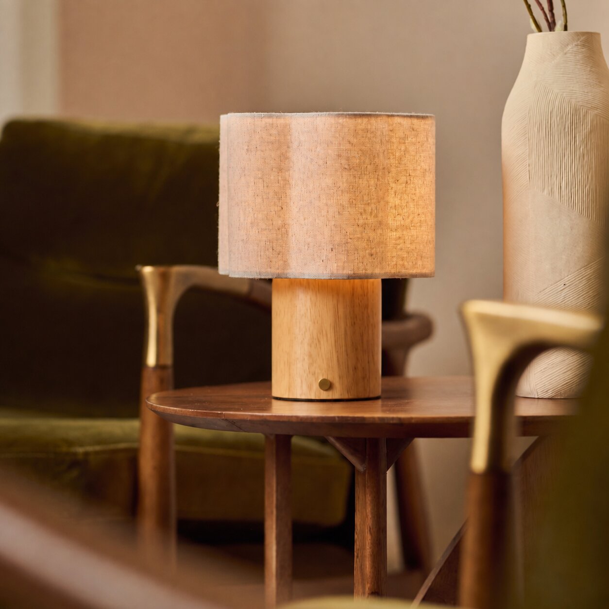 Lucy bois clair lampe de table sans fil Tavellio – abat-jour tambour en lin – près d'un canapé en velours vert olive