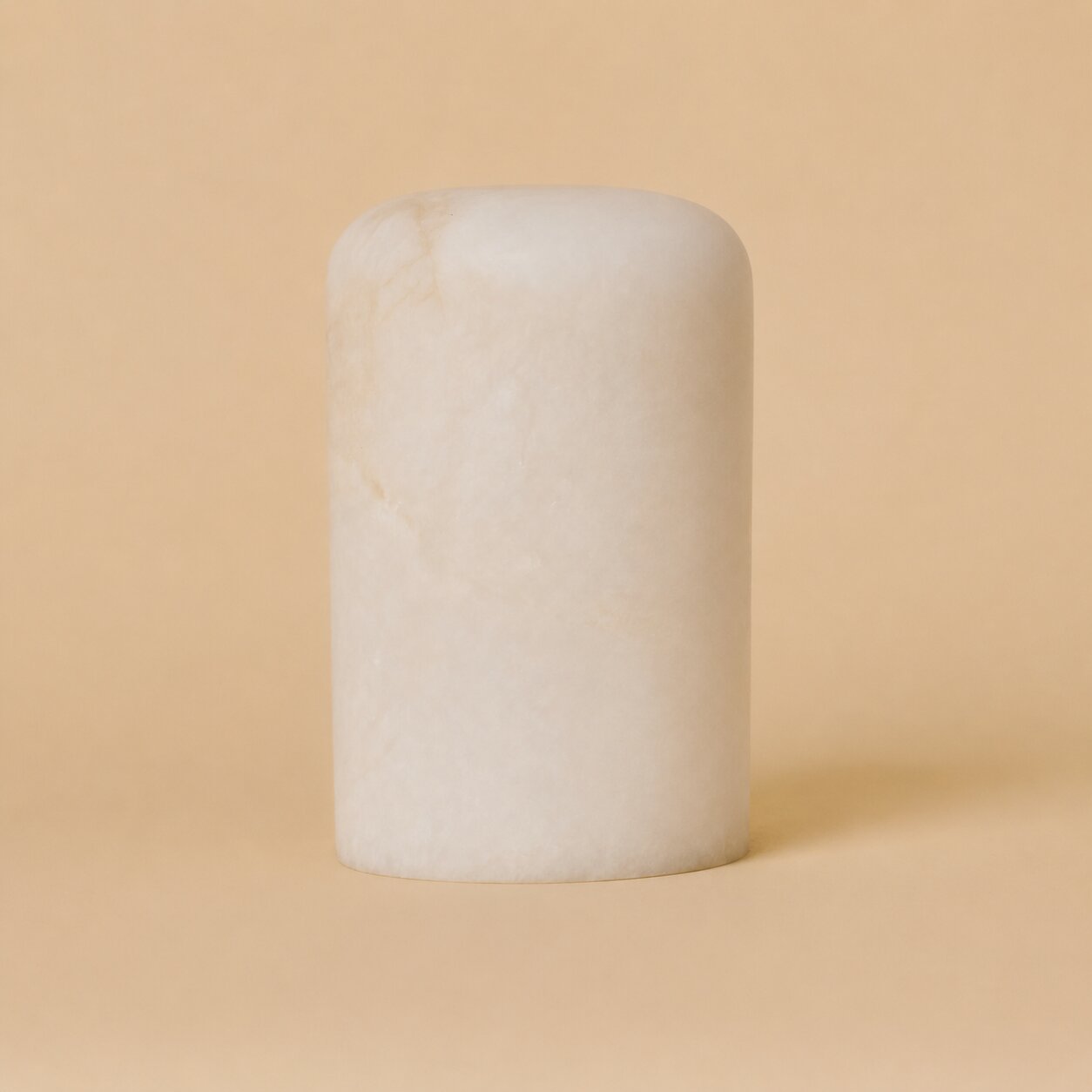 Rechargeable table lamp Tavellio Noé alabaster shade shown on its own, rounded cylinder against an ochre backdrop.