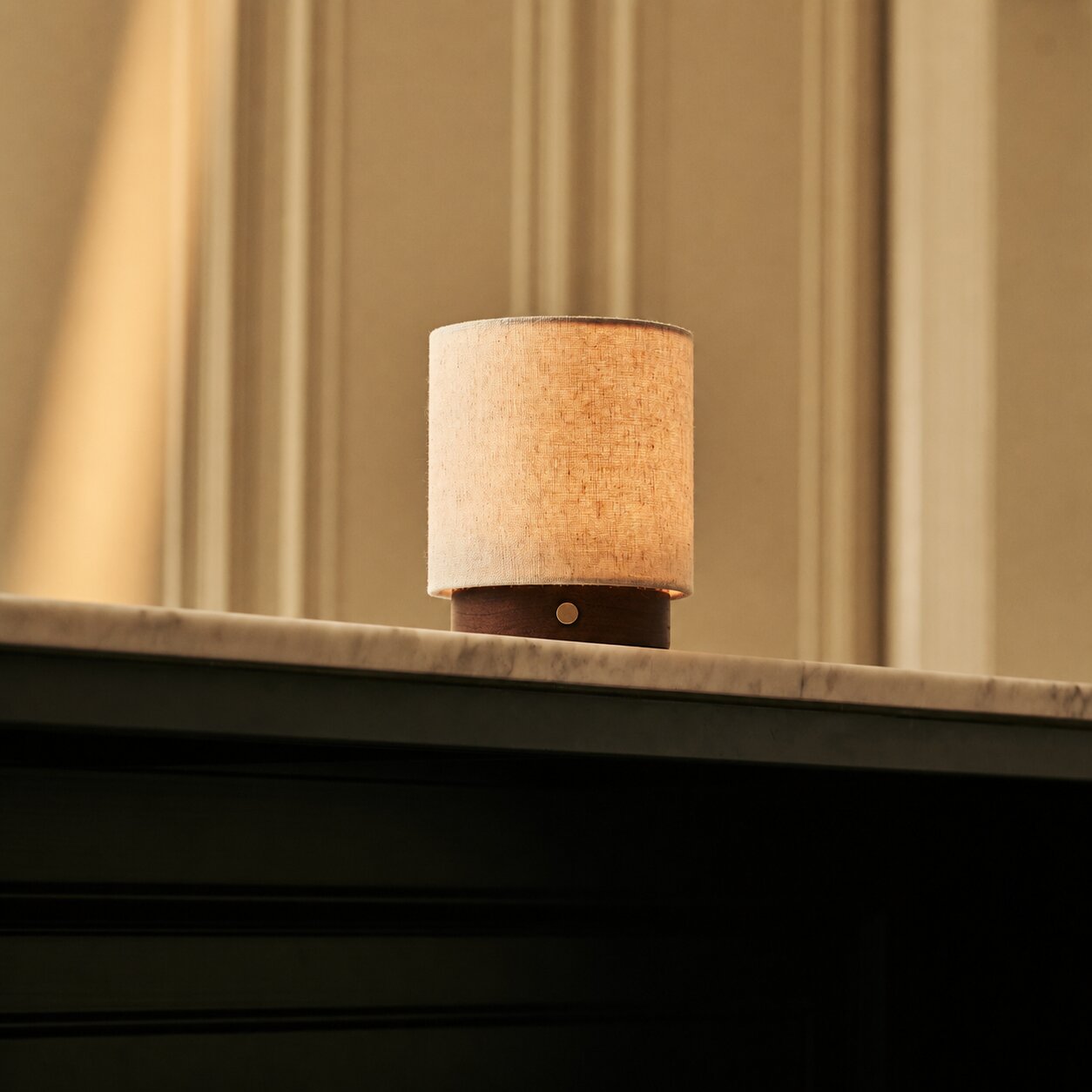 Oplaadbare tafellamp Dick Small Dark Brown, linnen kap op donker houten voet, op marmeren schouwrand