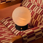 Oplaadbare tafellamp Flore Small zwart hout met glazen bolkap op een rood-wit gestreepte fauteuil