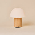 Cordless table lamp Ton with light brown wood base and frosted glass dome shade on a neutral background