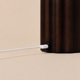 Gros plan sur le socle en bois cannelé brun foncé d'une lampe Tavellio – détail du connecteur de charge USB-C et de son câble blanc