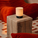 Oplaadbare tafellamp Dick Small in zwart met linnen kap op travertine bijzettafel naast bank